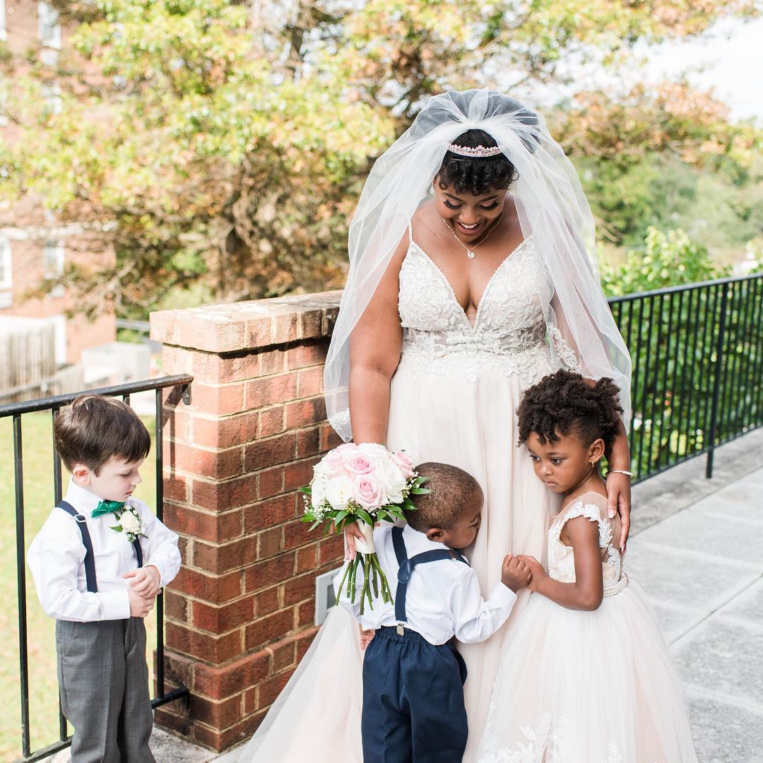 Bride in v-neck A-line wedding dress hugging flower girl and ring bearer