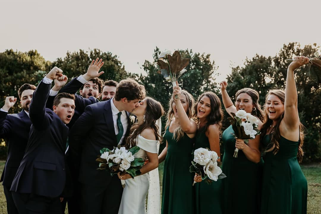 Bride and Groom kissing with bridal party cheering in background