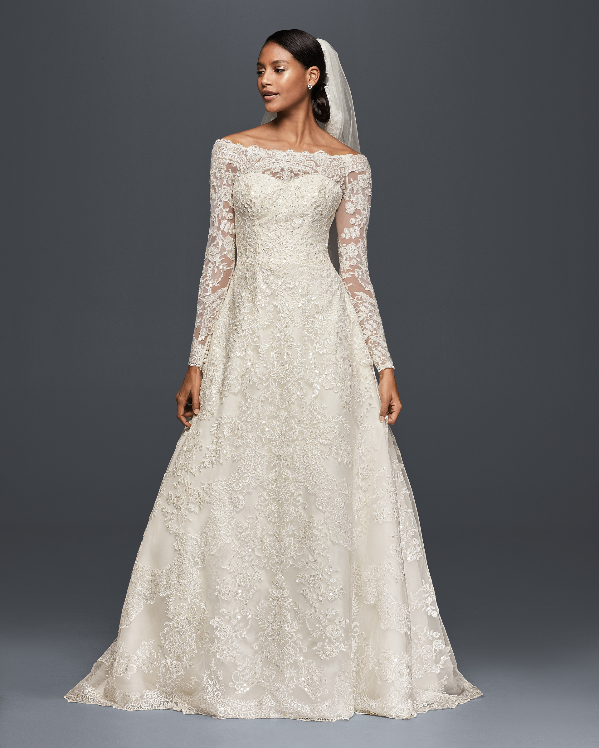 Bride in Meghan Markle wedding dress look a like A-line gown with off-the-shoulder neckline and long lace sleeves.