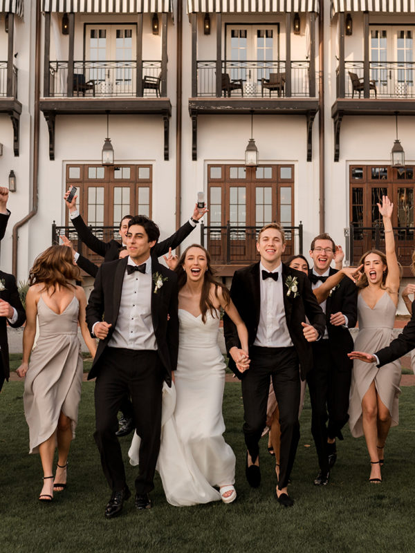 Bridal party holding hands and smiling, running on grass