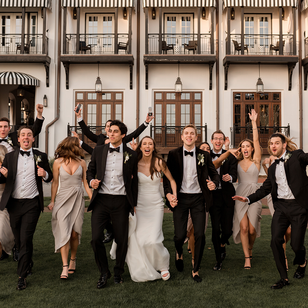 Bridal party holding hands and smiling, running on grass