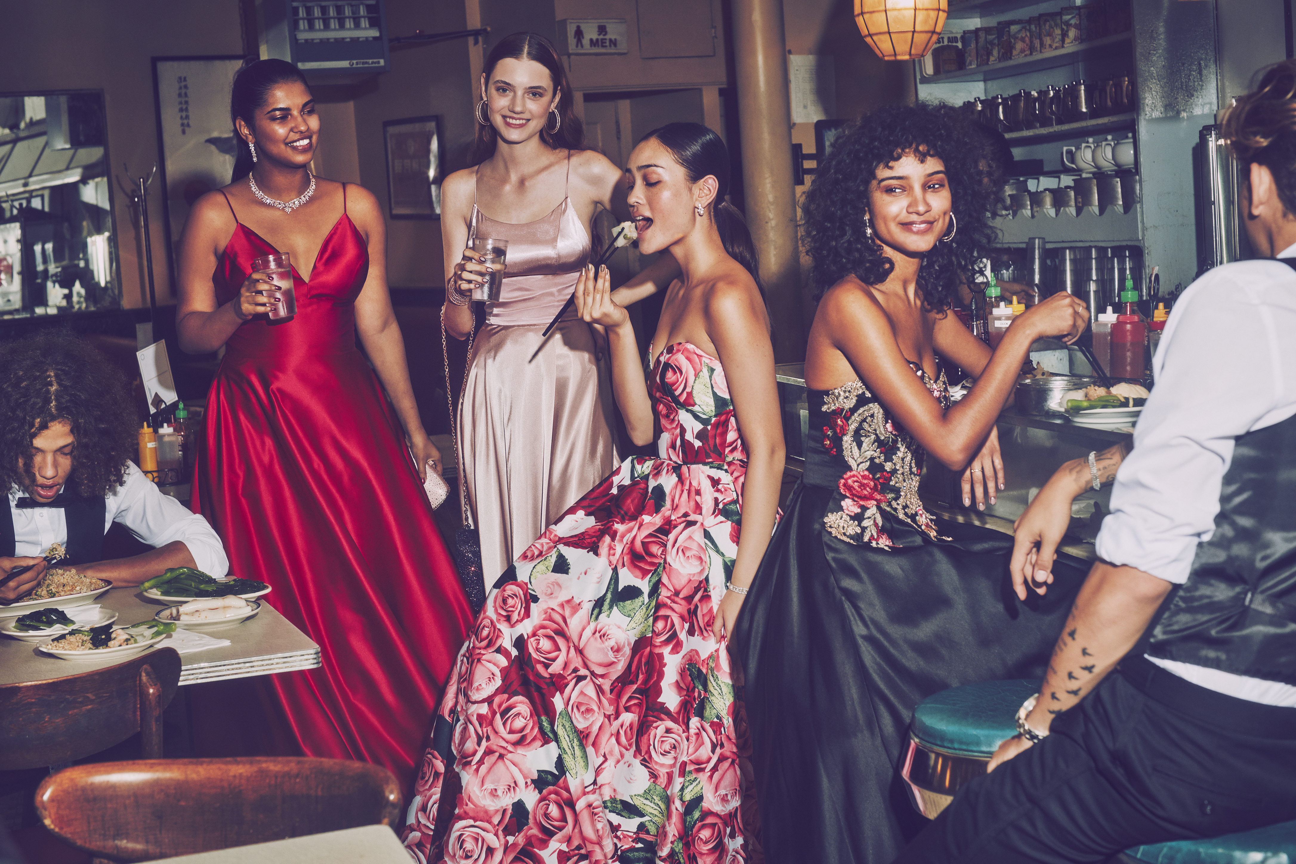 Girls in red, pink, floral print, and black prom dresses at a restaurant