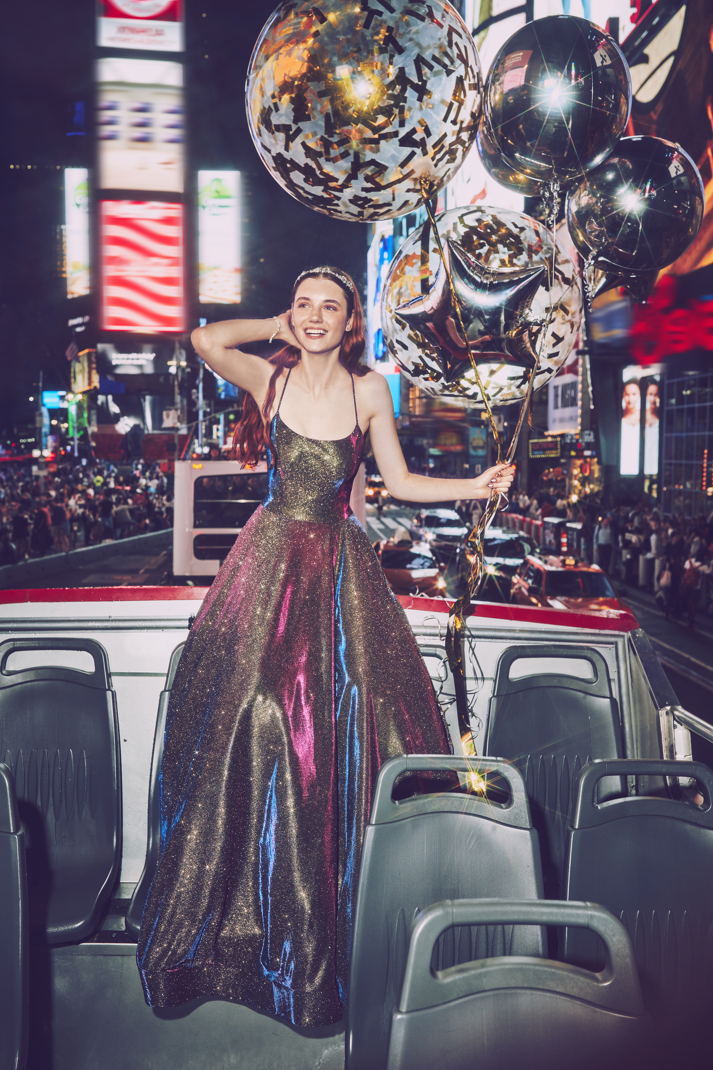 Girl in multicolored ball gown prom dress on a bus in Times Square New York holding balloons