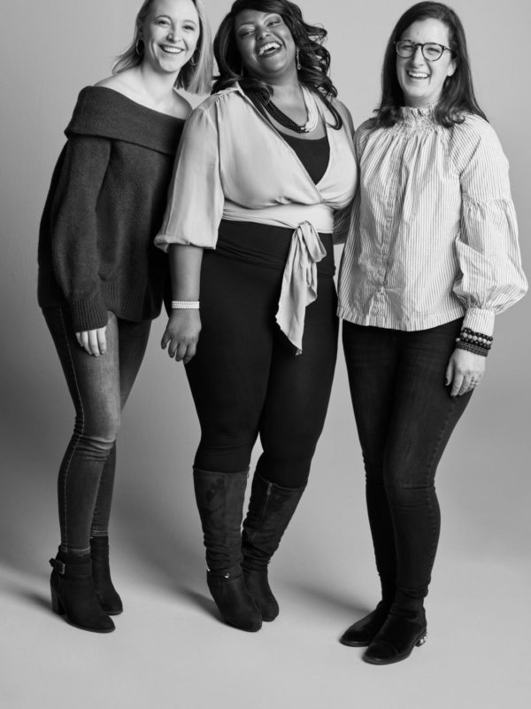 Three women from David's Bridal's Digital team smiling and pictured in a photo studio setting)