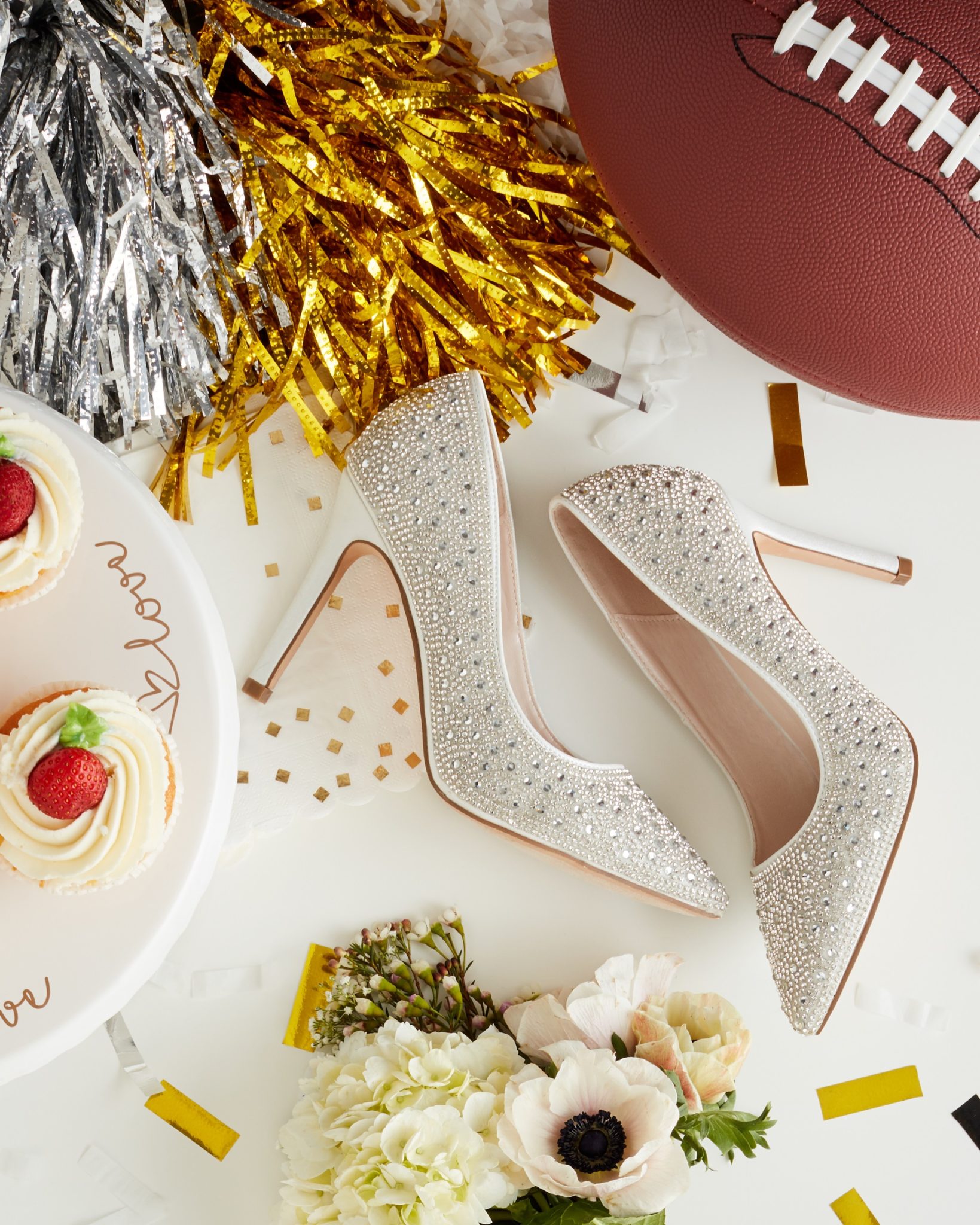 Flat lay with sparkly wedding heels, an all-white wedding bouquet, a football and gold and silver pom poms