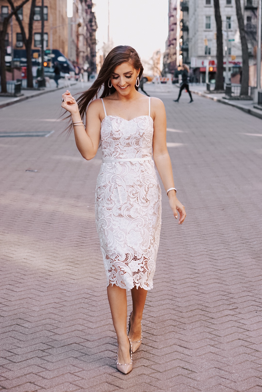 Woman in a short spaghetti strap lace dress standing on a brick road