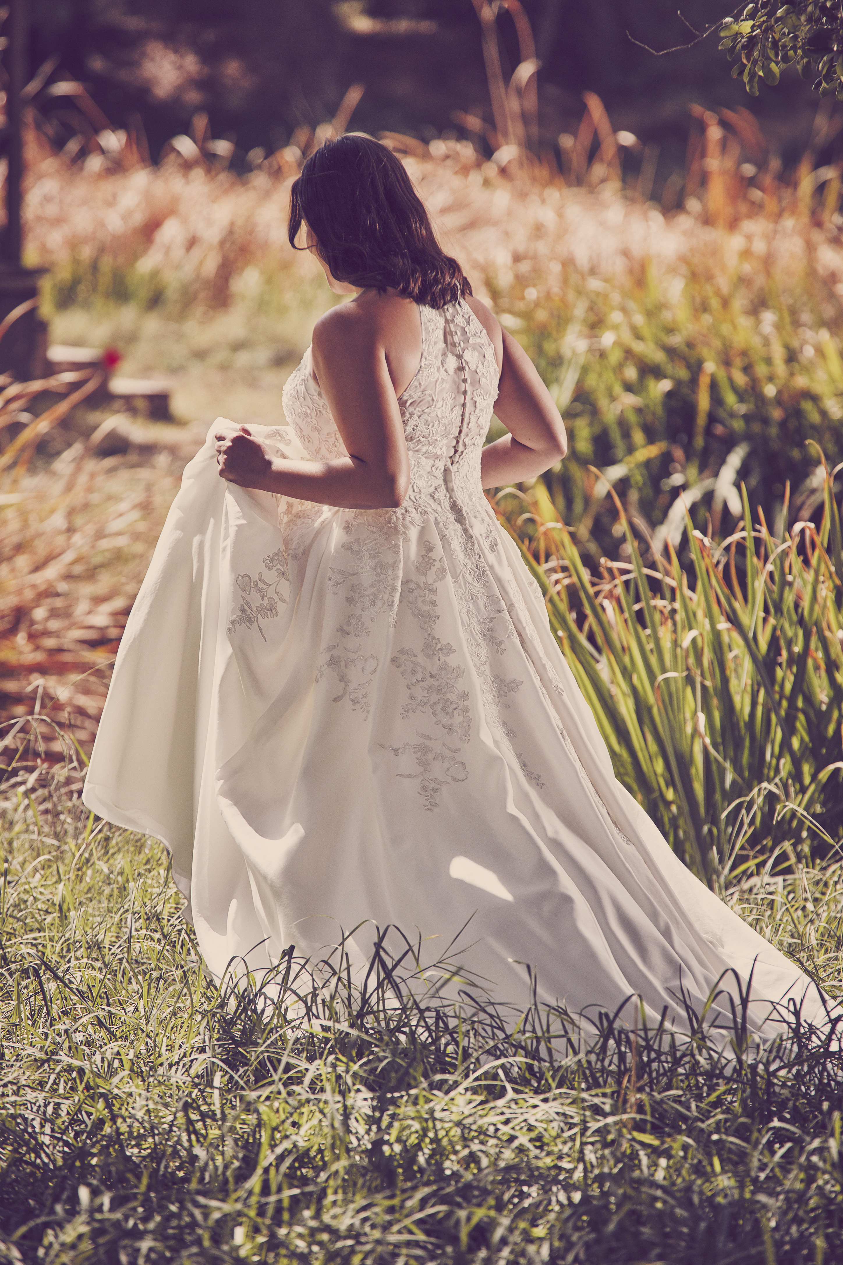 Woman walking in grass holding up skirt of ball gown wedding dress