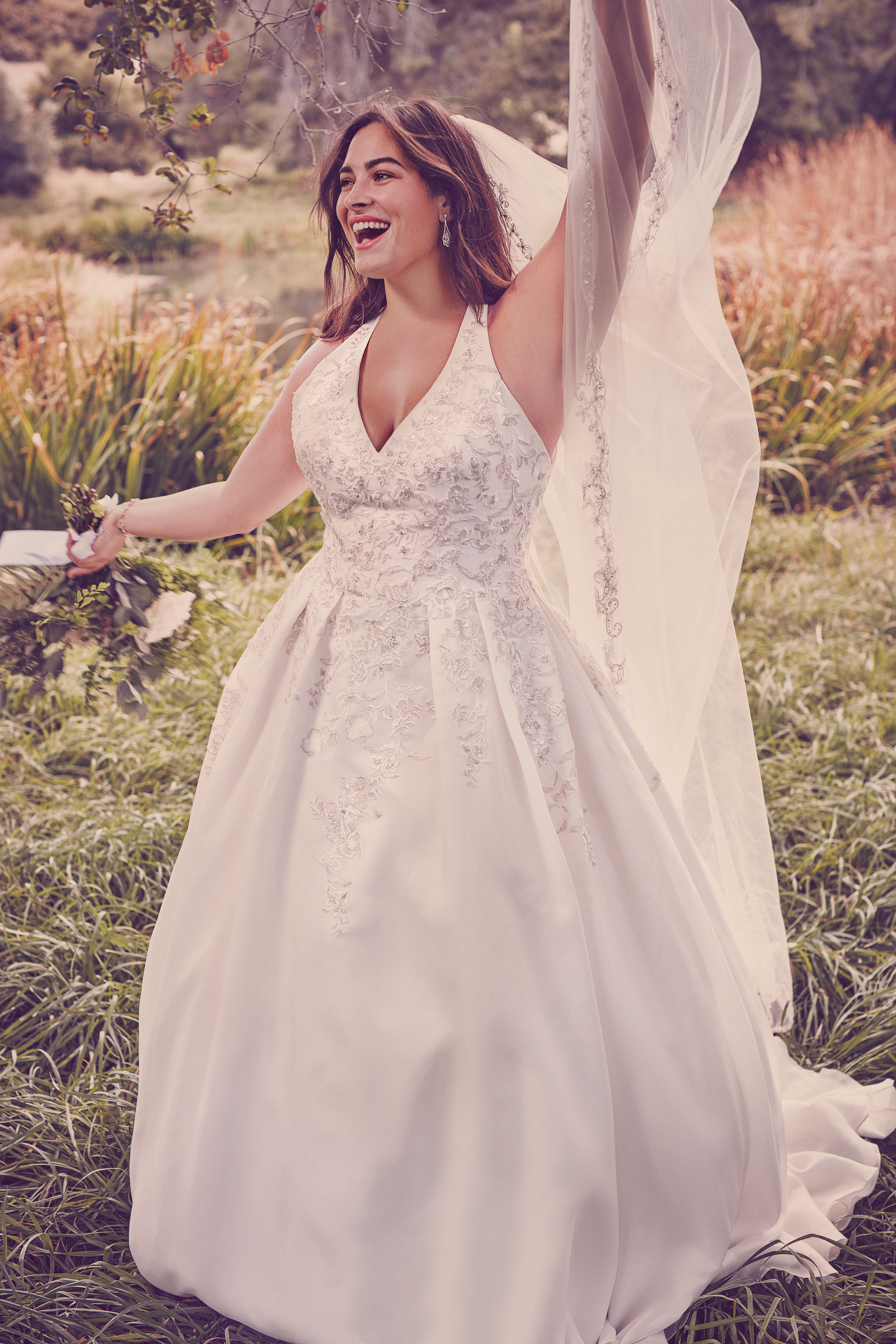 Woman in white wedding dress smiling and holding veil in the air