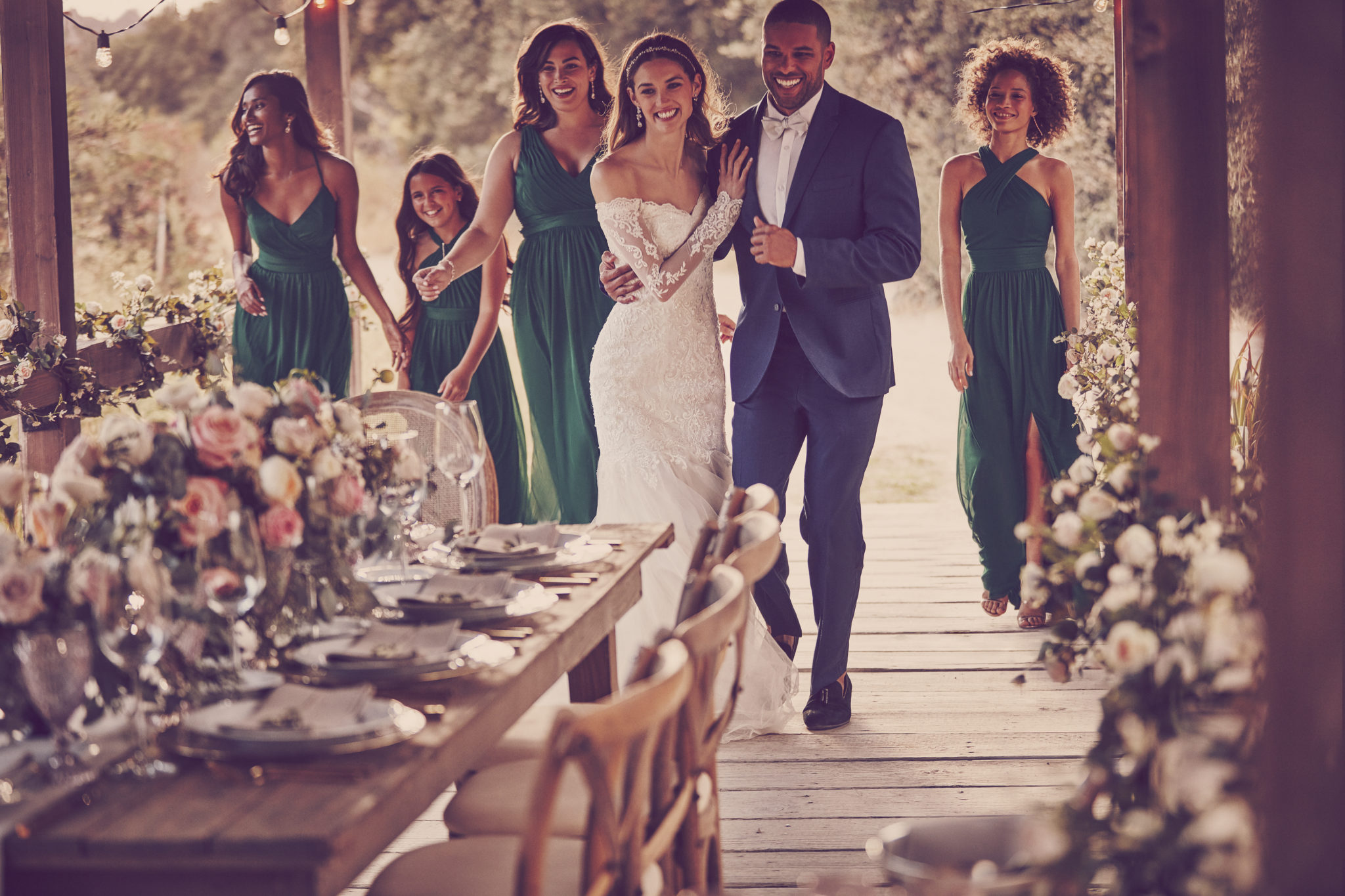 Women and man on walking on covered bridge towards a formal outdoor wedding