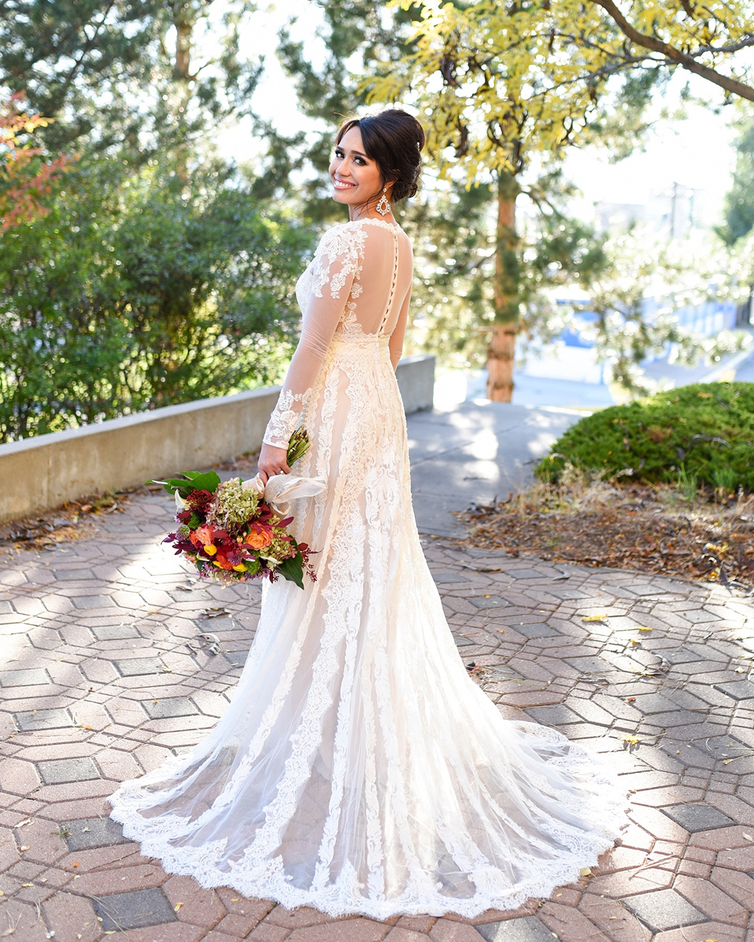 Bride in a long-sleeve lace gown showing off the back details of her dress in a garden setting.