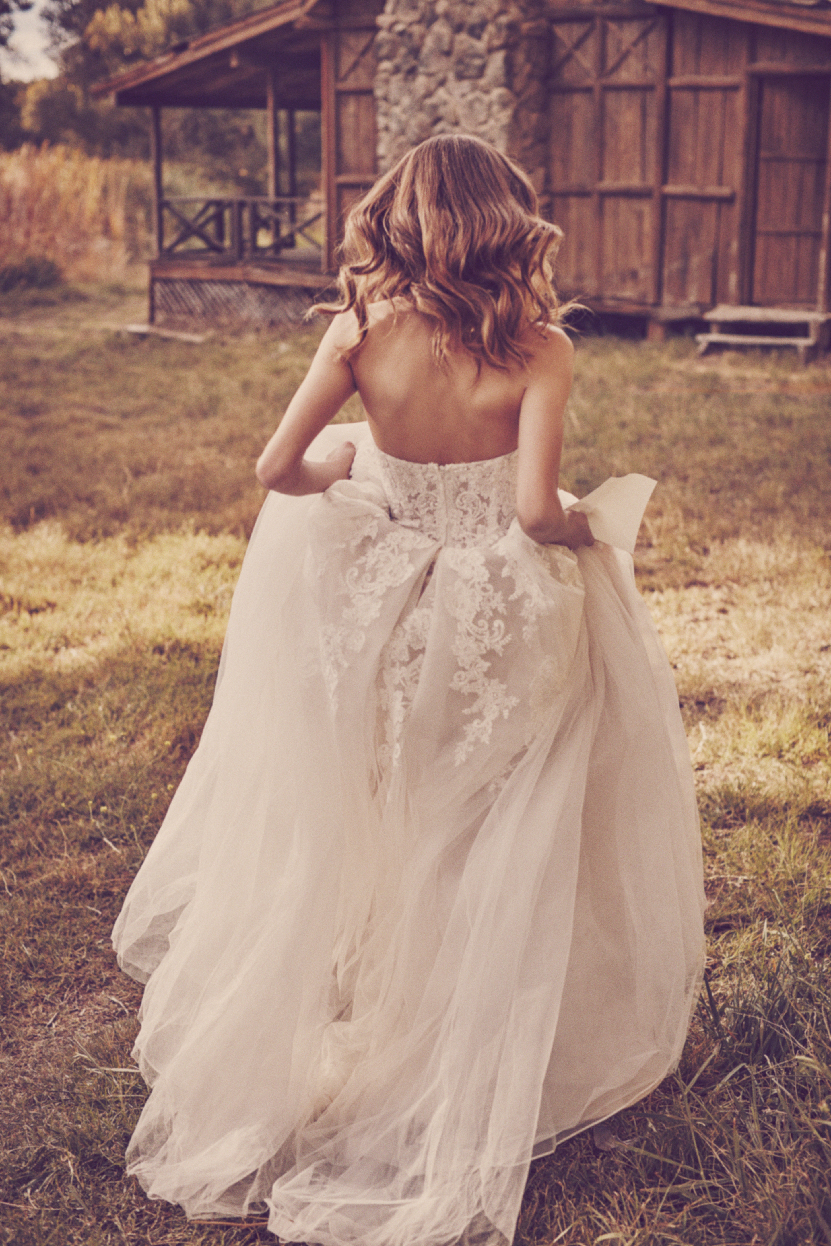 Woman running on grass holding up skirt of ball gown wedding dress