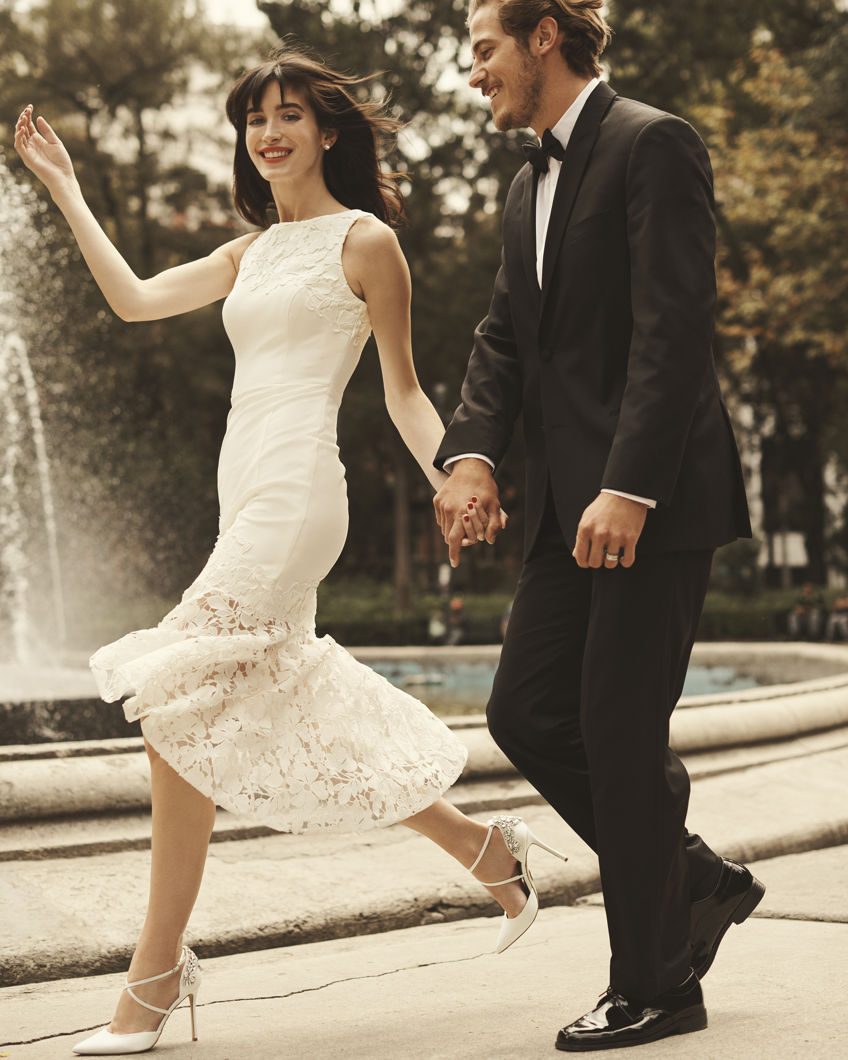 Bride in high-low lace wedding dress running hand in hand with groom in tux