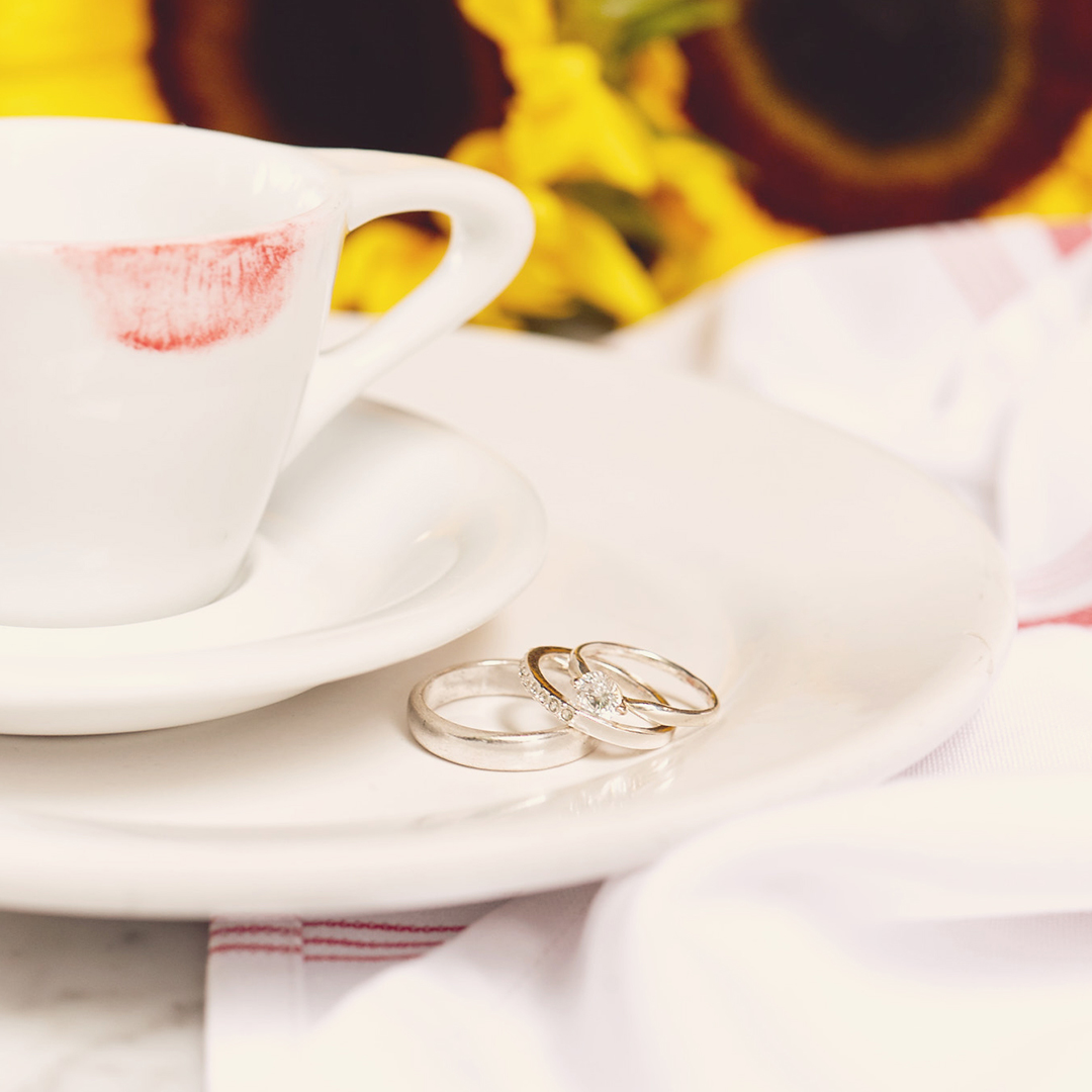 Espresso cup with red lipstick mark and silver wedding rings on plate.