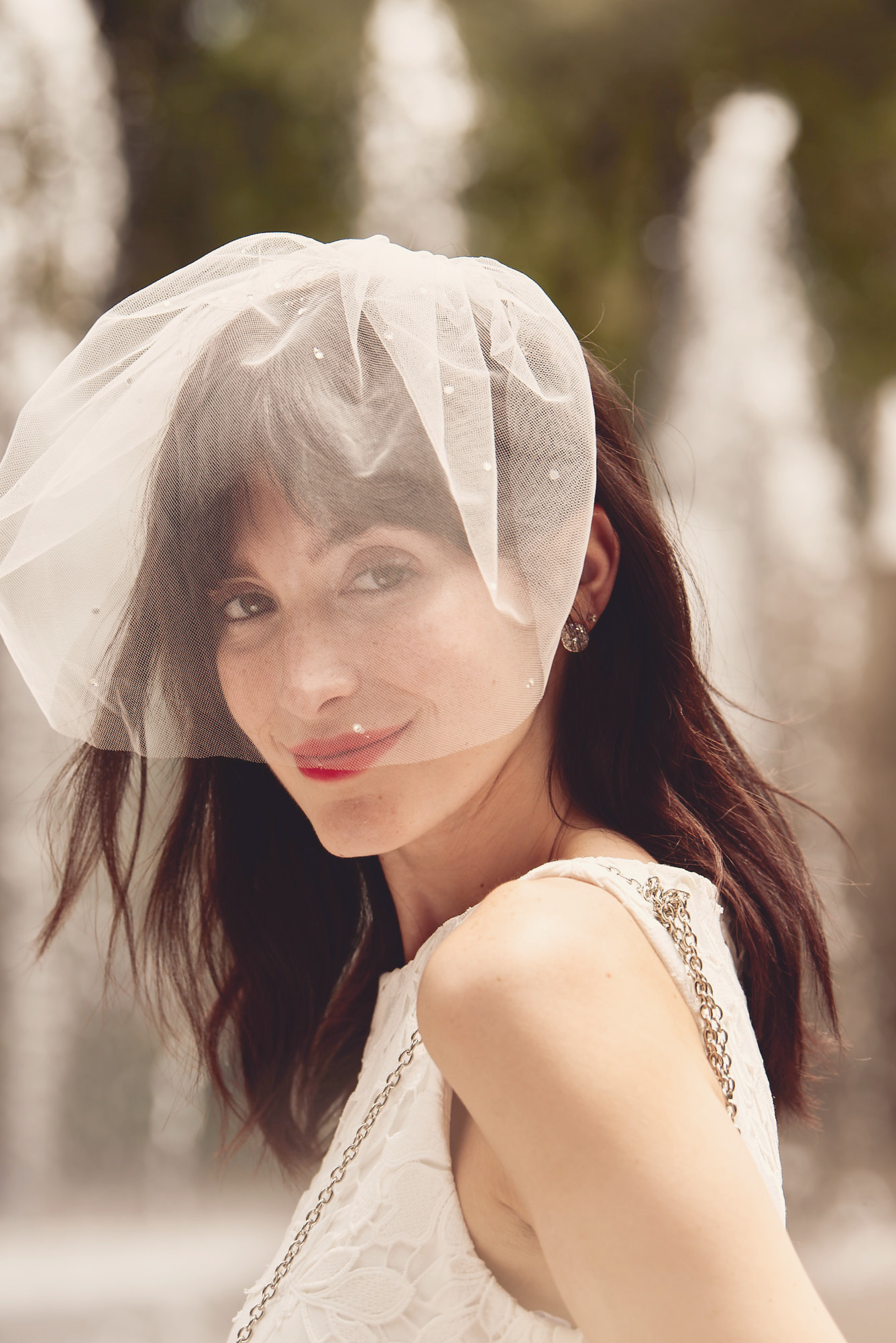 Smirking bride wearing tulle birdcage veil covering her face