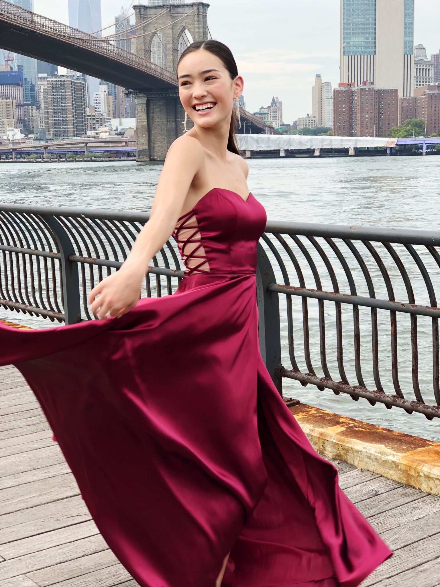 Girl in prom dress dancing on boardwalk at Brooklyn Bridge Park