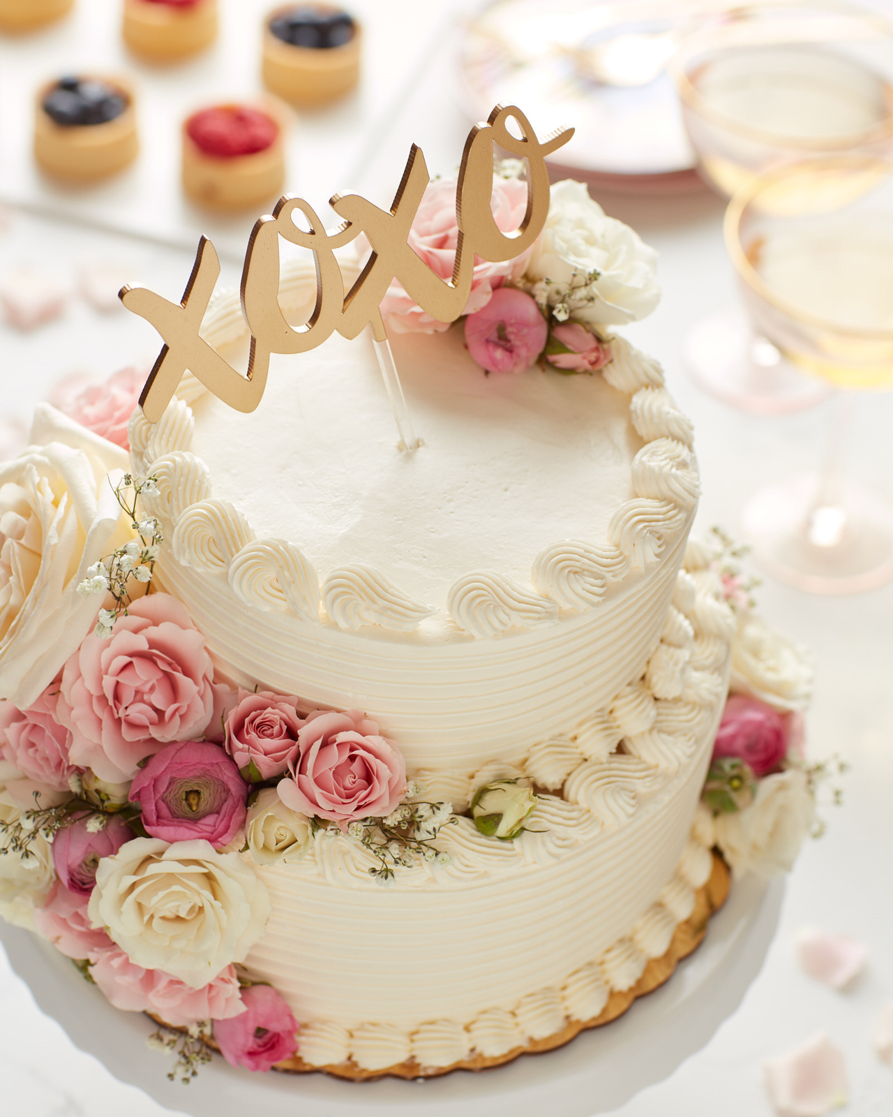 White two-tier wedding cake with pink and white flowers and a XOXO cake topper