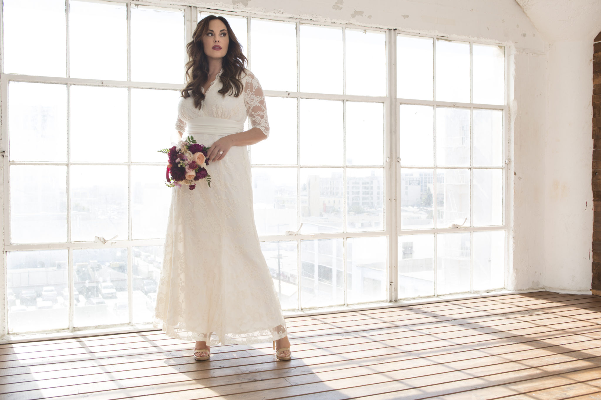 Bride in V-neck lace wedding dress with 3/4 sleeves against a wall of windows