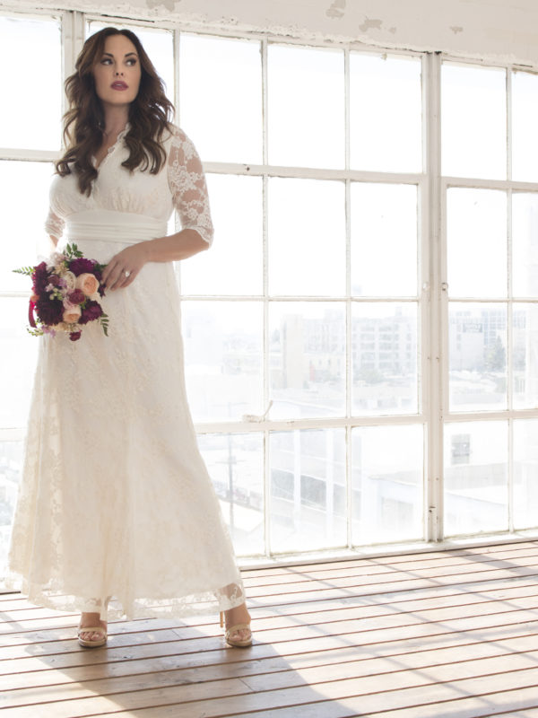 Bride in V-neck lace wedding dress with 3/4 sleeves against a wall of windows