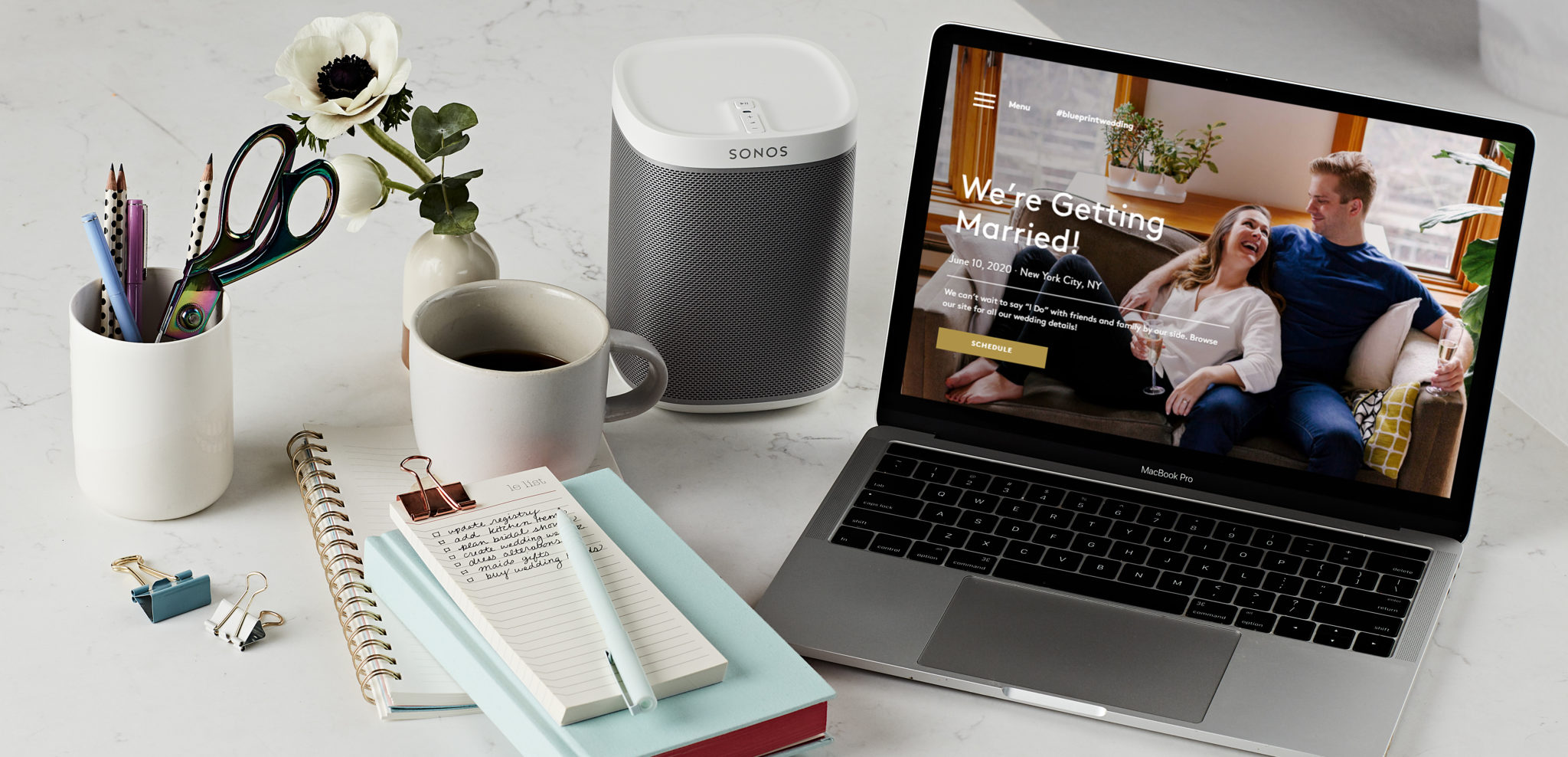 desk set up with pencil holder, mug, notebook, speaker and laptop displaying a wedding website