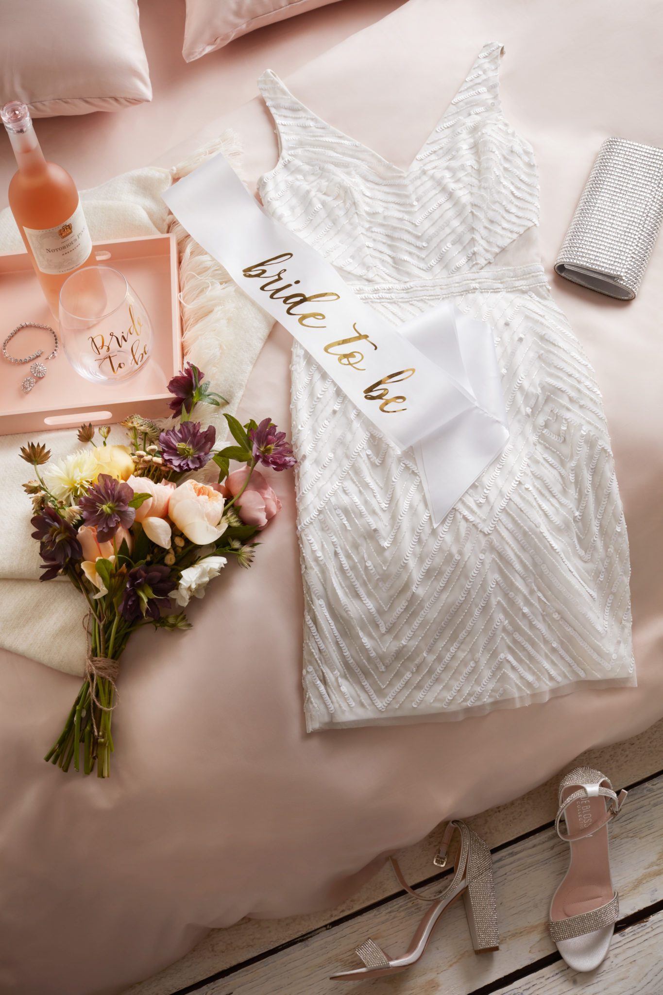 White dress laying on bed with flowers and tray of wine