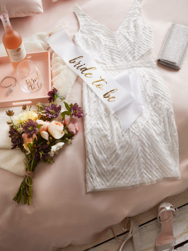 White dress laying on bed with flowers and tray of wine