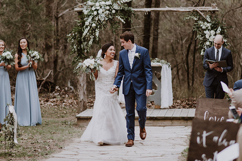 Bride and groom at an outdoor wedding ceremony in front of a wooden arch with white roses