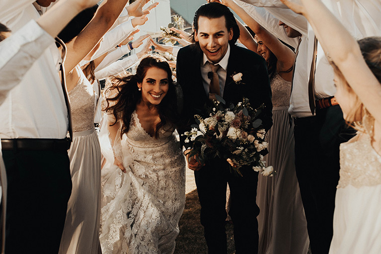 Bride and groom walking under archway with guests' hands raised