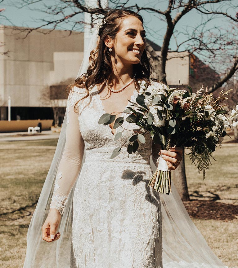 Bride in long sleeve lace wedding dress with a bridal bouquet filled with lush greenery and white flowers. 