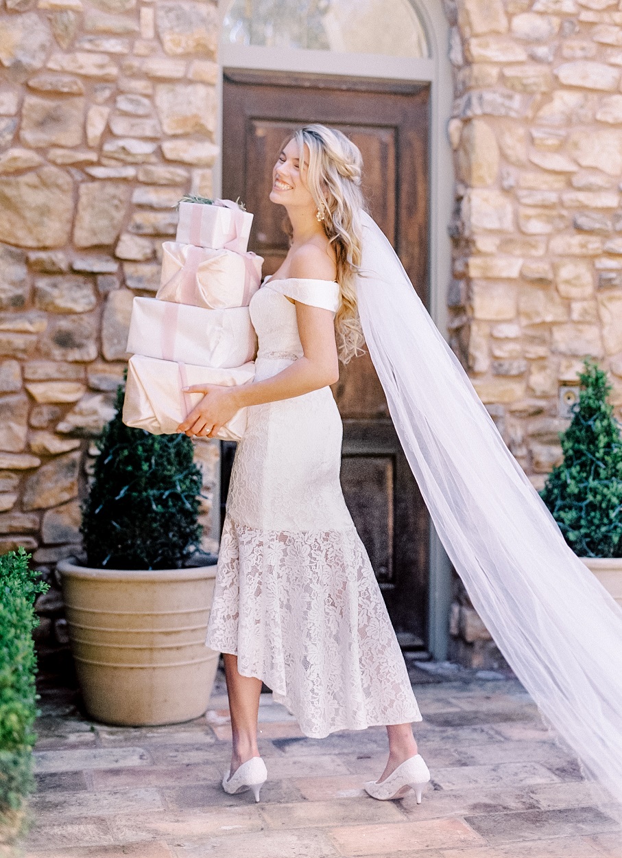Bride in short lace dress and long veil carrying gifts