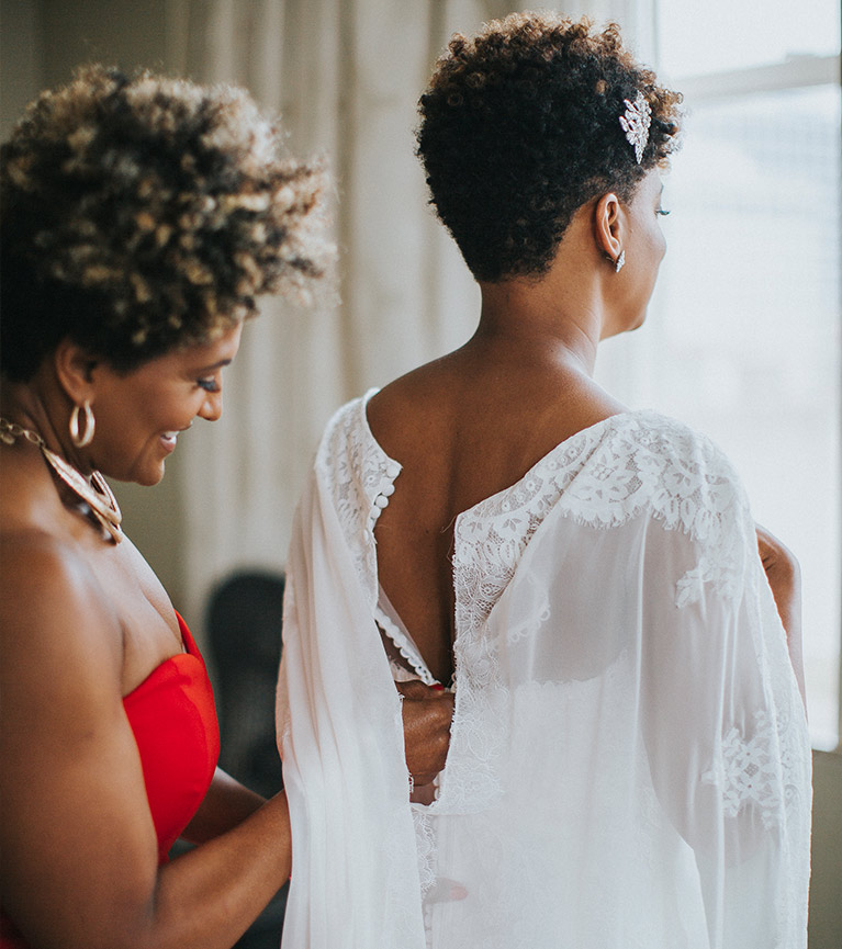 Mother of the bride helping her daughter button the back of her wedding dress