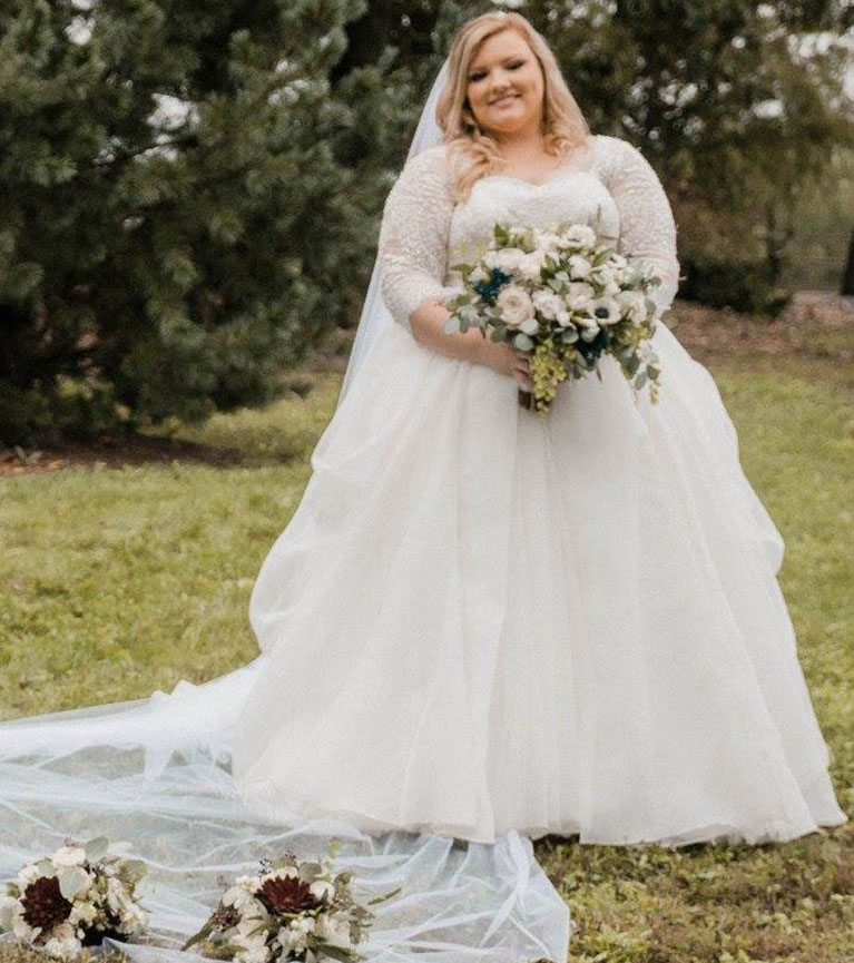 Bride in long sleeve lace ballgown holding a bouquet of white flowers with dark flowers mixed in. 