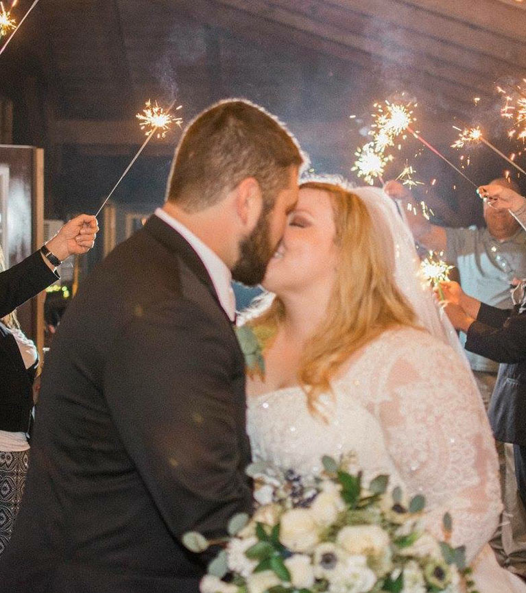 Bride and groom kissing as guests hold sparklers in the background. 