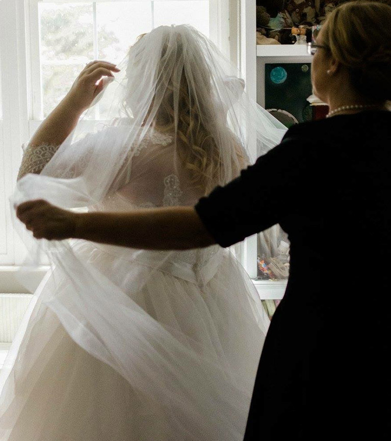 Mother of the bride helping a bride put on her veil - both from behind