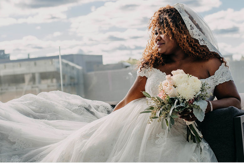 Bride sitting in an off-the-shoulder ball gown wedding dress with lace trimmed veil