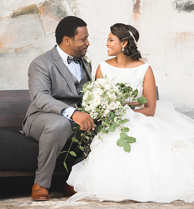 Groom and bride seated on a gray couch with modern artwork behind them