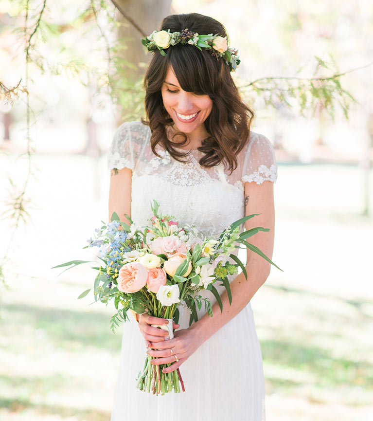 Bride in short sleeve lace wedding dress wearing a flower crown and holding a bouquet of peach flowers.