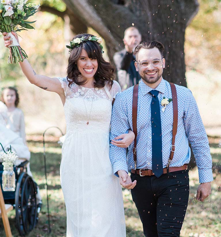 Bride and groom walking down the aisle as guests throw birdseed.