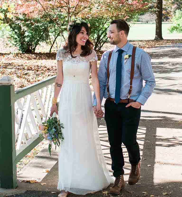 Bride and groom holding hands while walking through a park