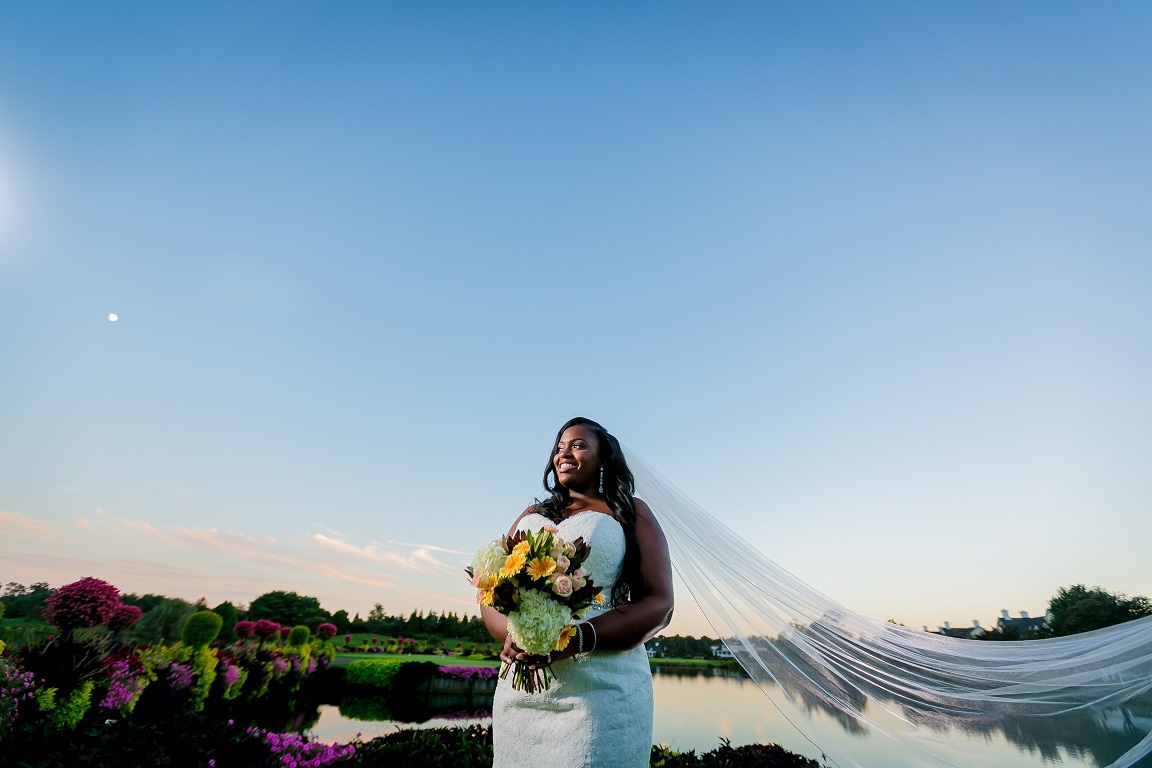 Bride holding a colorful bouquet near a pond with veil blowing in the breeze