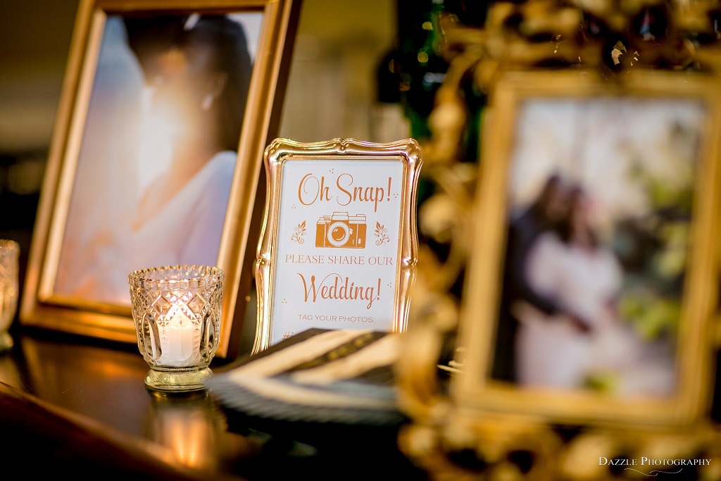 Wedding reception decor featuring family photos and wedding hashtag in vintage gold picture frames