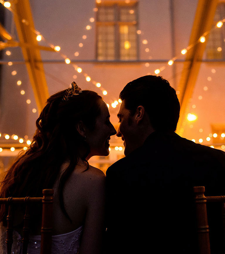 Bride and groom seated and going in for a kiss with twinkling lights behind them