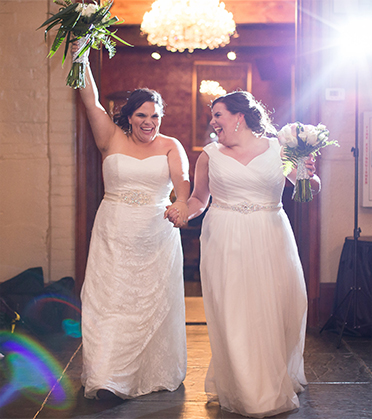 Two brides holding hands as they enter through a door. 