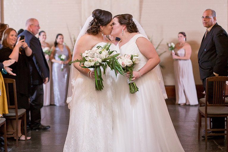 Two brides kissing at their wedding ceremony.