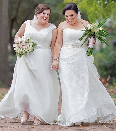 Two brides laughing and holding hands. 