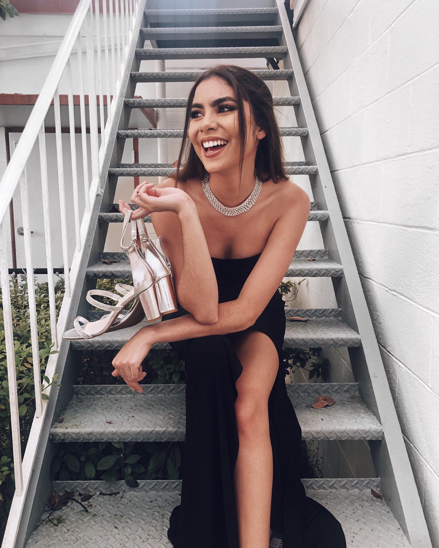 Girl in long black strapless dress sitting on stairs holding heels