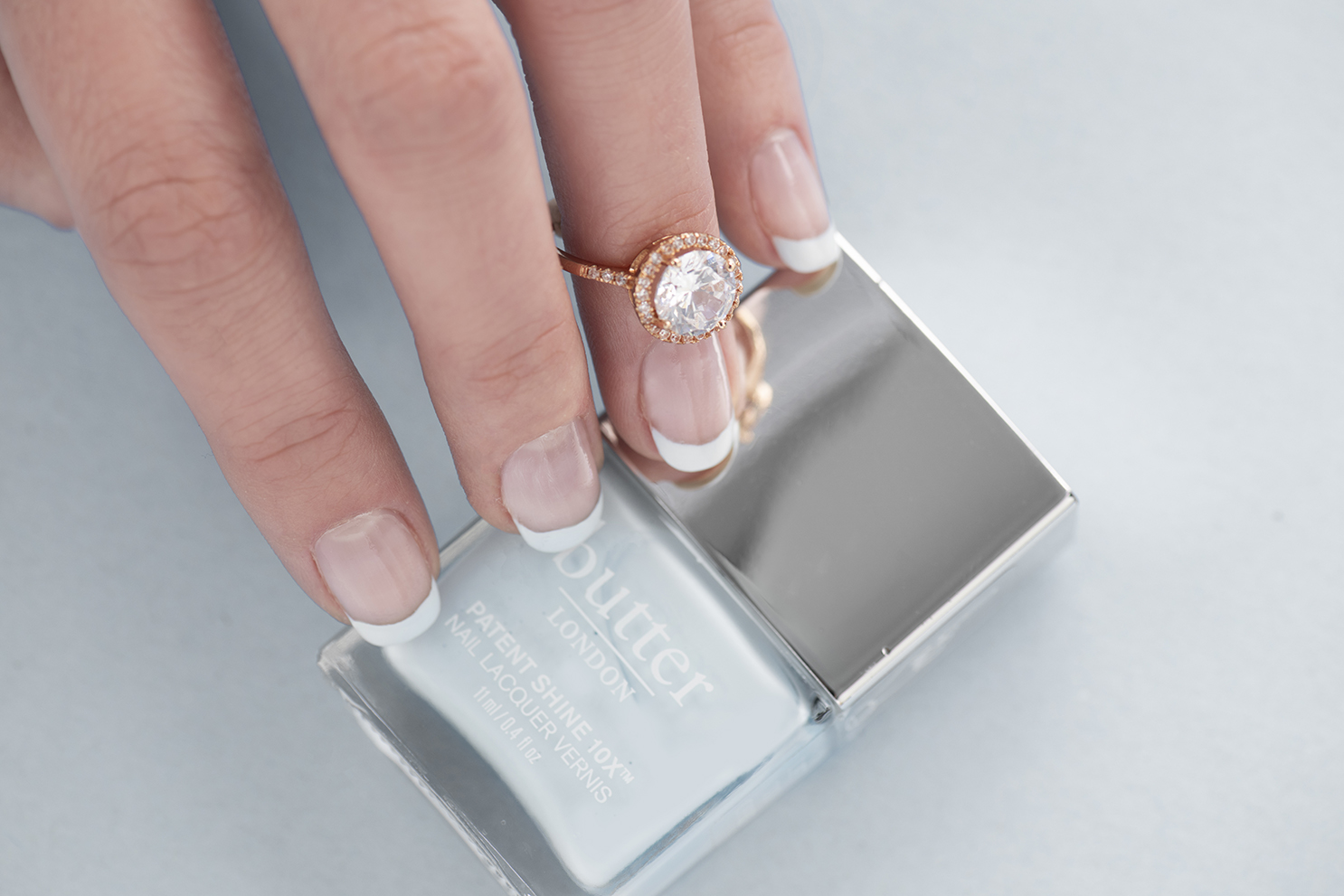 A woman with a French manicure holding a nail polish bottle.