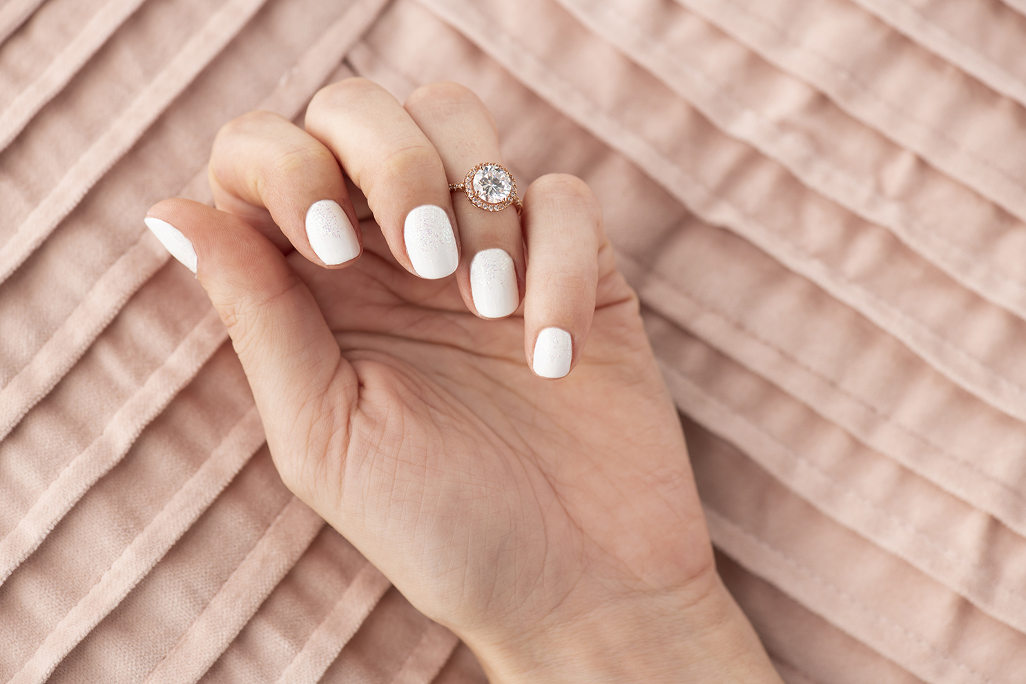 A woman's hand with a white and glitter manicure.