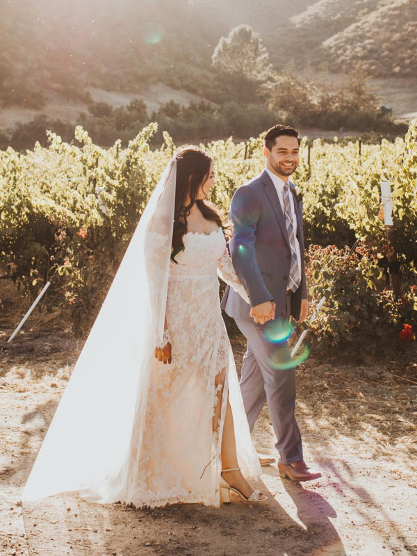 bride in a floral lace wedding dress walking with groom