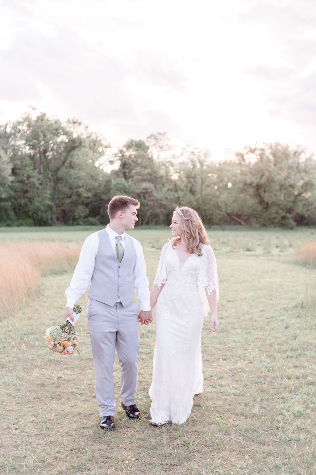 bride and groom looking at each other walking hand in hand in a field at dreamy springtime wedding
