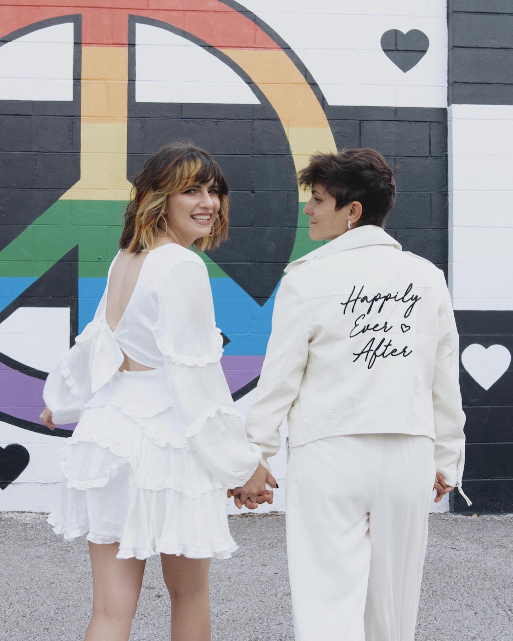 brides walking wearing a little white dress and a jumpsuit with a jacket